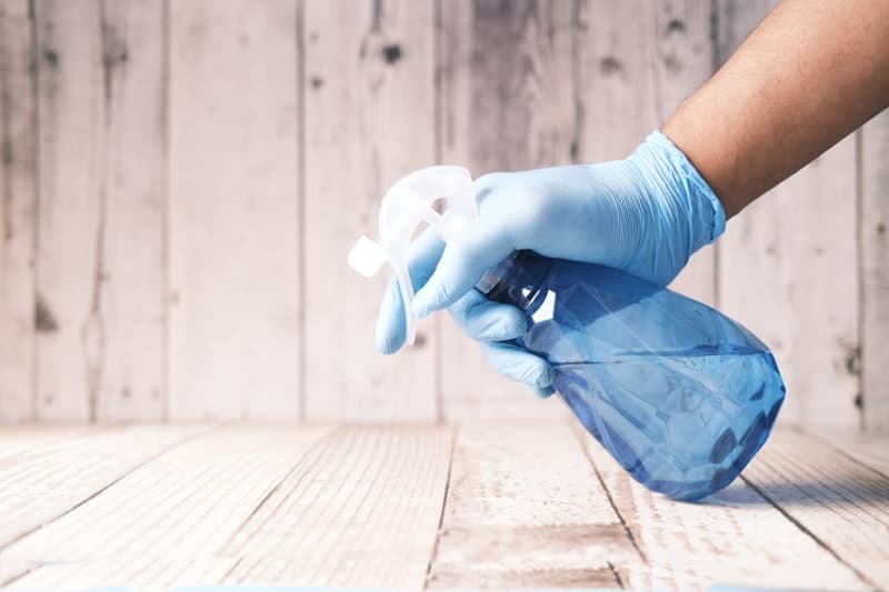 Gloved hand spraying cleaner along a wooden floor