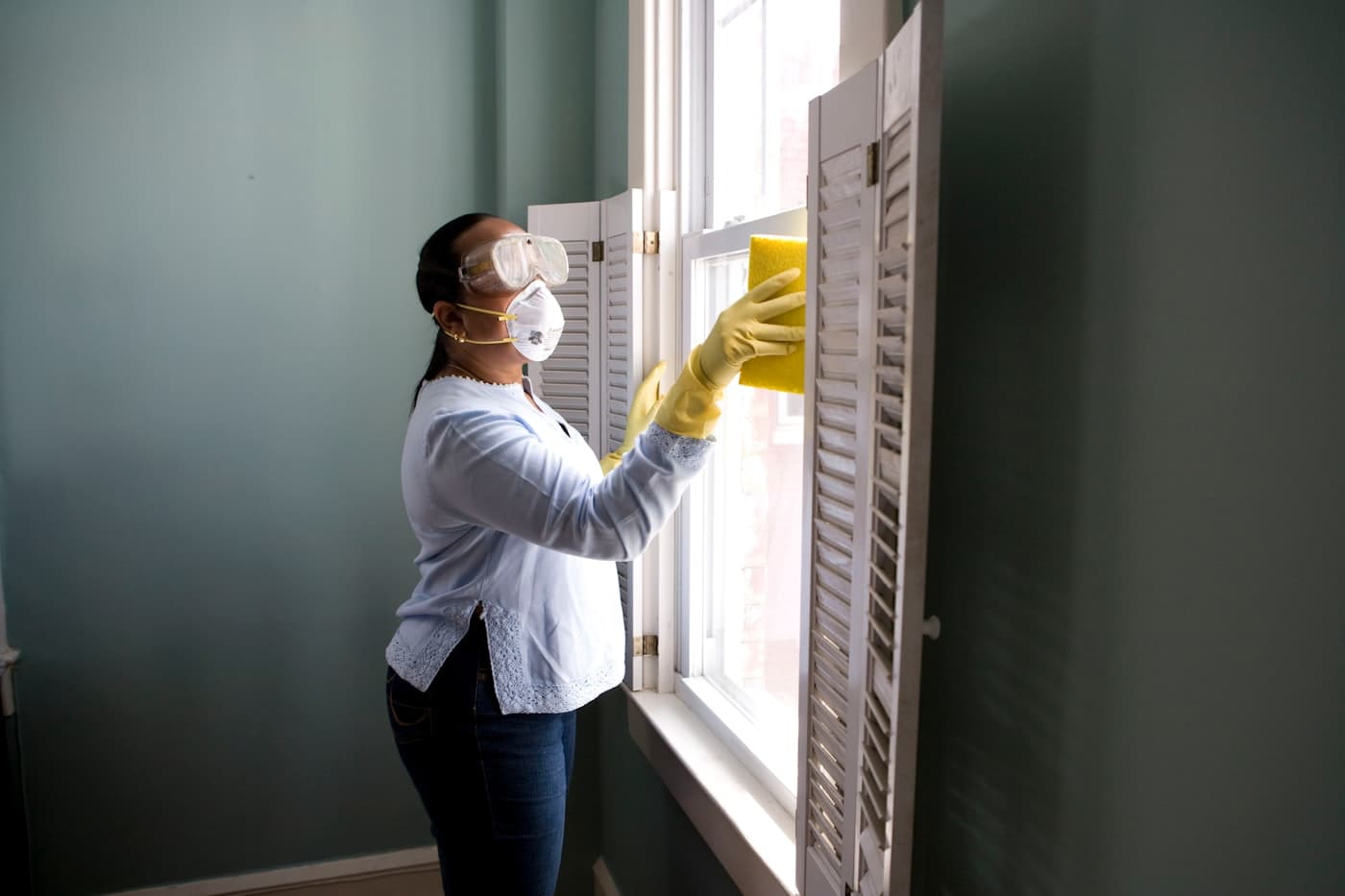 Cleaner in gloves washing a bright window with a yellow sponge